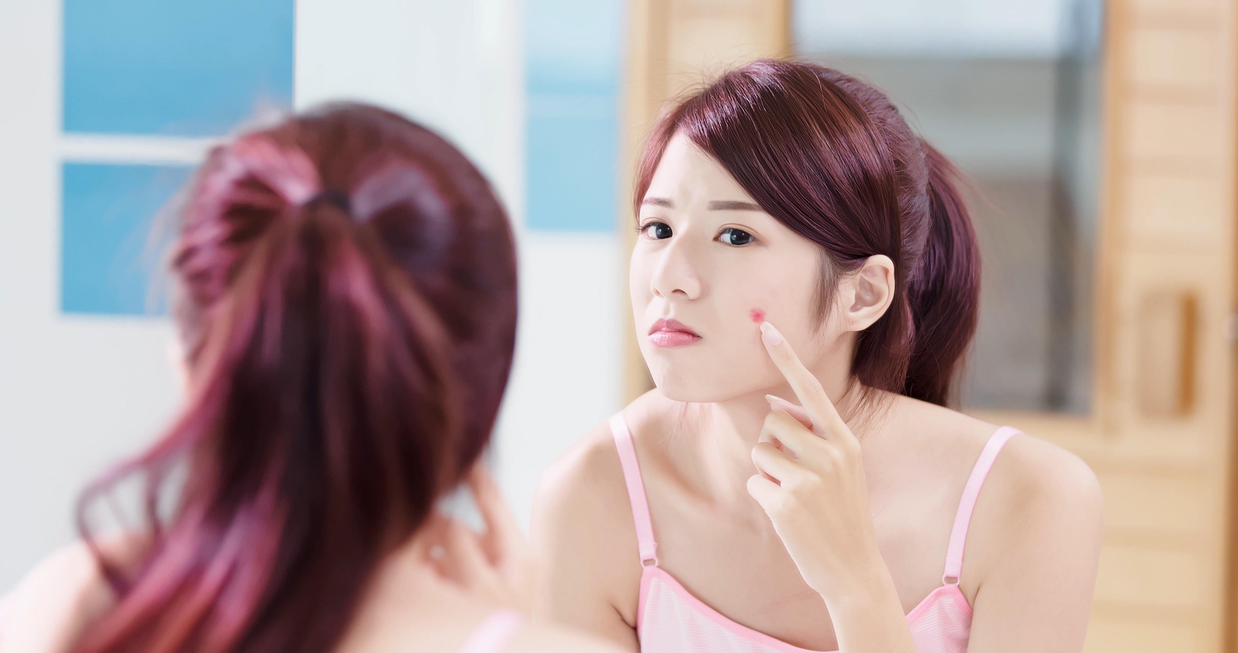 girl with pimple looking in mirror